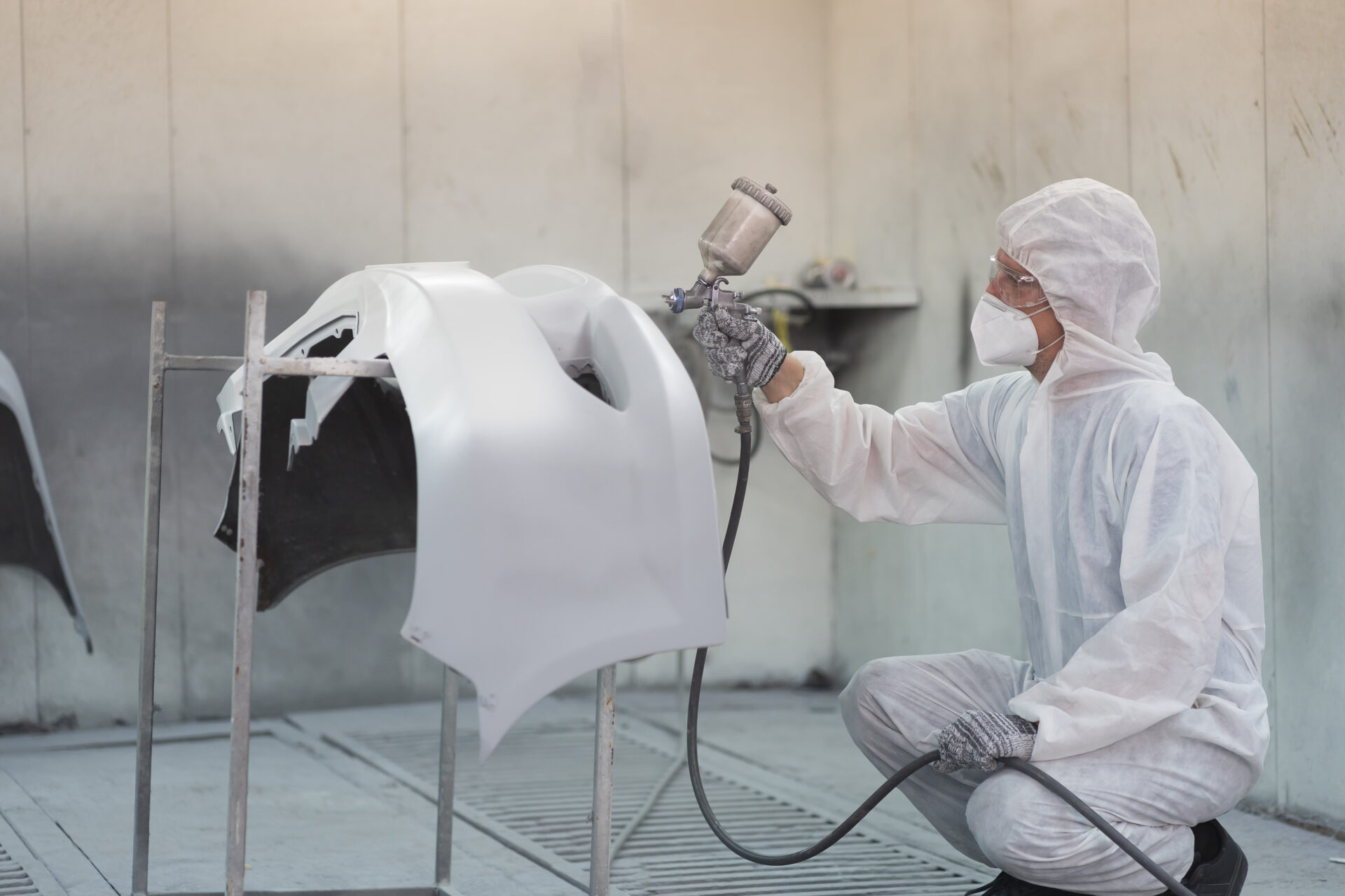 Automotive paint service. Quality auto body shop concept. Male car mechanic working with spray gun painting auto body in automotive paint service shop. Automobile painter painting car frame in chamber AdobeStock 597557149